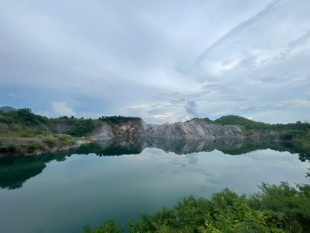 Calm quarry lake with clear reflection of rocky cliffs and green vegetation, creating a peaceful and minimalist natural landscape.の写真素材