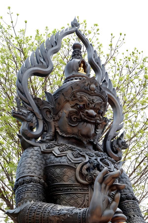 Ornate temple guardian statue in Asian style featuring intricate carvings and dramatic expression, surrounded by natural foliage.の写真素材