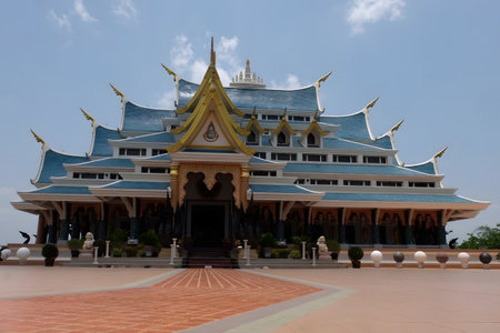 Front view of a traditional Thai Buddhist temple featuring elegant blue roof tiles and golden architectural details. Symmetrical design with open courtyard under a clear blue sky. Concept of religion, spirituality, culture, heritage, travel, and sacred architecture.の写真素材
