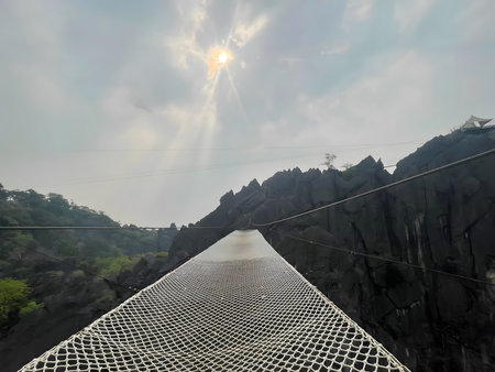 Suspended net bridge stretching across dramatic rocky cliffs under soft sunlight. The perspective creates a powerful sense of adventure, risk, courage, and forward movement, symbolizing challenge, success, and personal growth.の写真素材