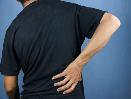 Close-up rear view of man's hand touching back pain, low back pain concept.
