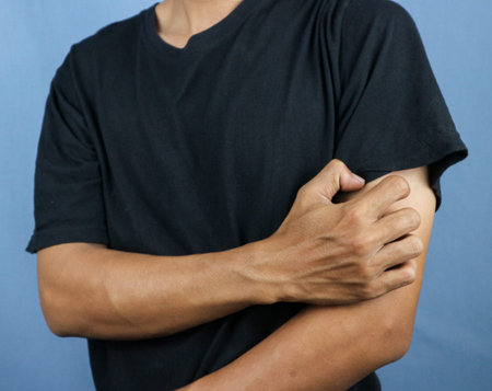 Asian young man scratching his hand isolated on blue background. Concept of itchy skin diseases such...