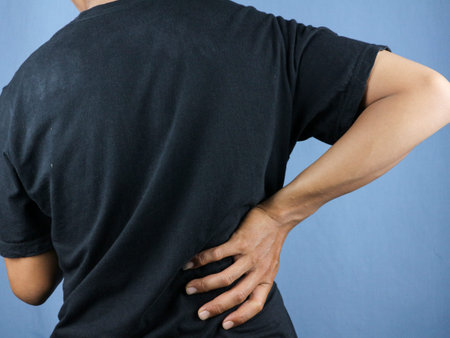 Close-up rear view of man's hand touching back pain, low back pain concept.