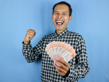 Excited expression handsome asian man hold paper money banknotes with clenched fist gesture....