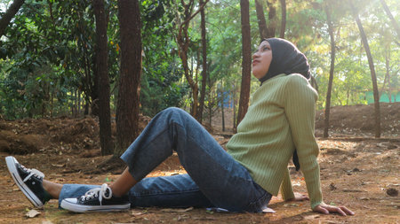 Young muslim woman resting carefree, relaxing on lawn on sunny day. Side view hipster woman with...