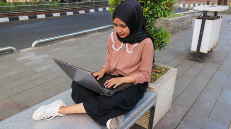 Portrait of Arab business Women working on laptop sitting at city park. Freelancer muslim woman using laptop for work. Copy spaceの写真素材
