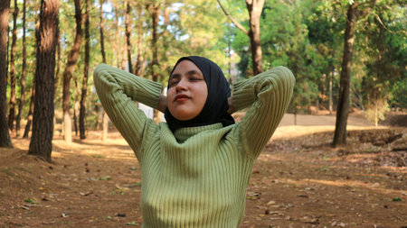 Smiling muslim woman with hands behind head and eyes closed breathing fresh air in middle of pinewood forestの写真素材