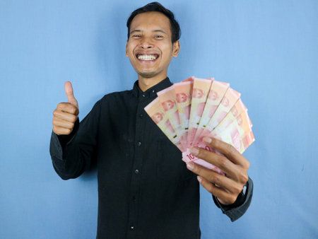 Excited expression handsome asian man hold paper money banknotes with thumps up gesture. Business and finance concept.の写真素材