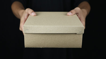 hands of delivery service man delivers carton box on black background. Cargo shipping, fast express...