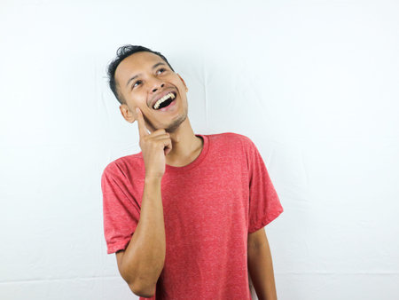Asian man touching chin thinking, making decision, choosing something, having doubts, standing on...