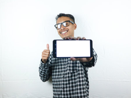Portrait of asian man holding big blank screen hand phone while giving thumbs up with smiling expression. Advertising conceptの写真素材