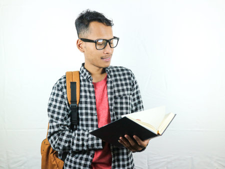 Handsome Asian student smiling and holding and reading book in hand