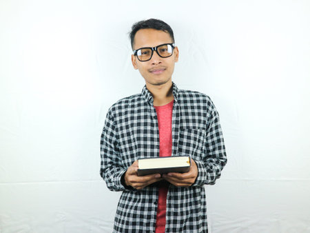 Handsome Asian student smiling and holding and reading book in hand