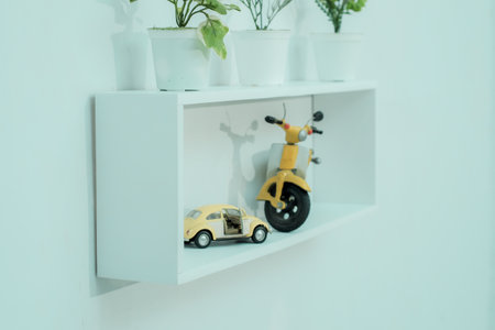 Wooden shelves with beautiful plants, alarm clock, toy cars and books on a light wallの写真素材