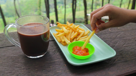 french fries, sauce, milk, chocolate on a wooden table with natural scenery as a background.