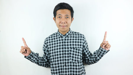 Adult Asian man wearing plaid shirt smiling while looking and pointing up side.の写真素材
