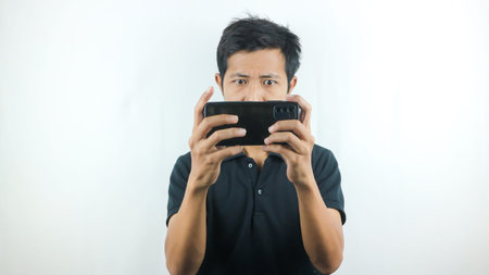 Asian man with a serious expression is playing a game on his cell phone.