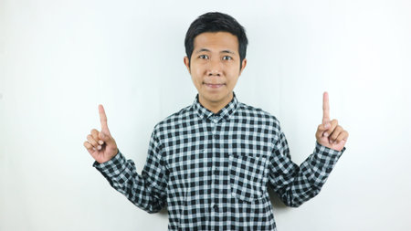 Adult Asian man wearing plaid shirt smiling while looking and pointing up side.の写真素材