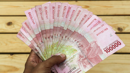 A man's hand holds a hundred thousand rupiah note. Asian young woman in black coat transacting...