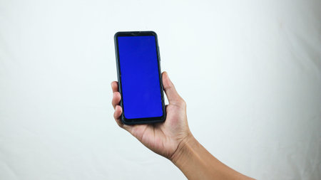 Asian man holding big smartphone with white, red, green, blue blank screen in hand, showing close to camera and pointing at device. Gadget with empty free space for mock up, bannerの写真素材