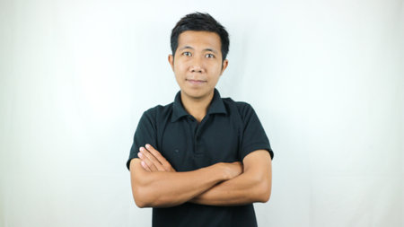 Smiling Asian man wearing casual black polo shirt with crossed arms looking at camera studio shot isolated on white background.の写真素材