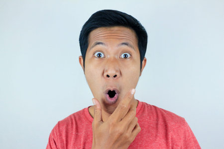 funny expression of shocked and surprised Asian man wearing a red t-shirt looking at the camera