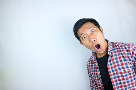 funny expression of shocked and surprised Asian man in flannel shirt isolated on white background