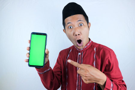 Surprised expression of asian muslim man holding phone and pointing on empty screen.の写真素材