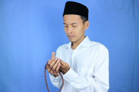 Muslim asian man holding prayer beads on blue background. Ramadan kareem and ied mubarak concept.