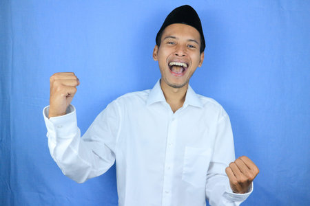 Portrait of overjoyed muslim asian man screaming with joy and clenched fists