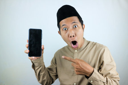 funny facial expression asian muslim men wearing cap while pointing empty phone screen.の写真素材