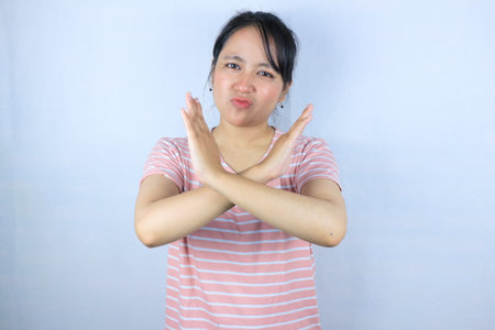 serious face expression asian woman showing crossed hands gesture and looking at camera while standing isolated over white backgroundの写真素材