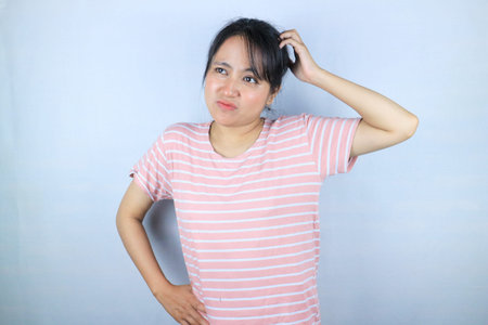 Confused expression of beautiful Asian woman scratching her head while looking up