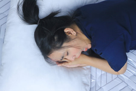 Tired beautiful Asian woman yawning in bed.の写真素材
