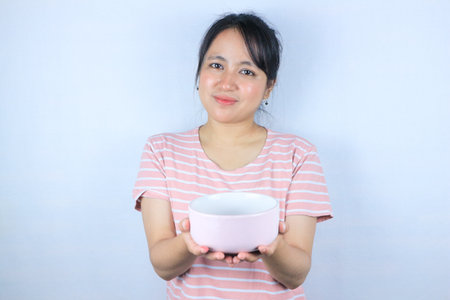 smiling expression of young asian woman looking at the camera while showing an empty bowlの写真素材
