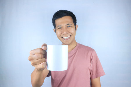 Smiling expression young asian man wearing t-shirt holding coffee cup, isolated on white backgroundの写真素材