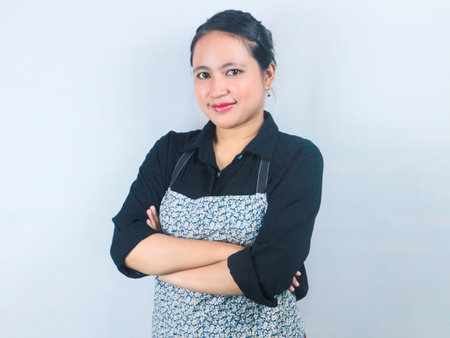 Portrait of beautiful Asian woman wearing apron with crossed arms gesture on white backgroundの写真素材