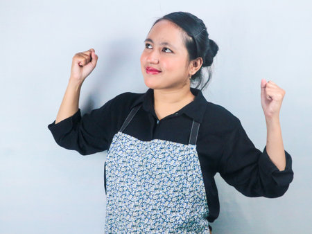Excited young asian woman wearing apron doing winner gesture clenching fistsの写真素材
