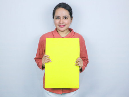 beautiful asian woman hold a blank yellow sheet in her hands. Smiling woman expresses her opinion or shows an interesting proposal. Place for text.の写真素材