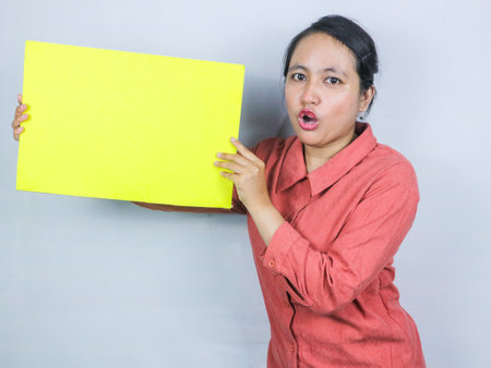 beautiful asian woman hold a blank yellow sheet in his hands. Smiling woman expresses her opinion or shows an interesting proposal. Place for text.の写真素材