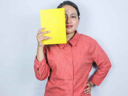 beautiful smiling asian woman holding a book covering half her face