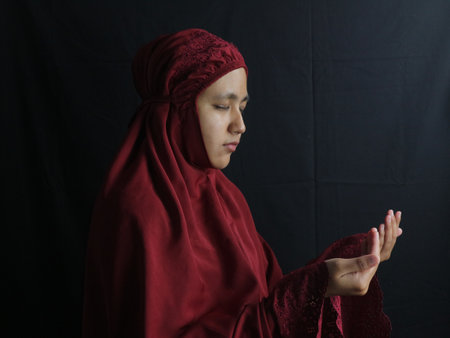 Side view of a muslim woman wearing mukena praying while hold prayer beadsの写真素材