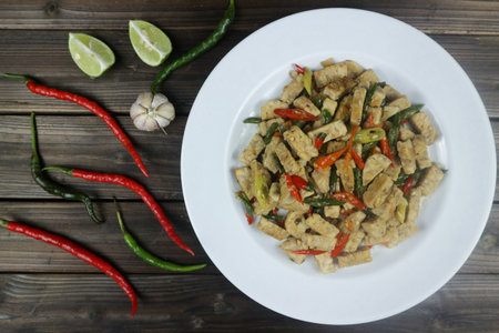 Oseng tempe or stir fry tempe with chili on white plate, against plank wooden backgroundの写真素材