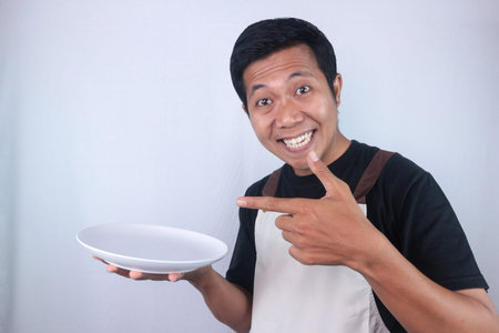 Excited face expression asian man chef or waiter shows empty white plate, presenting something....