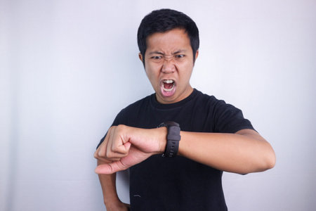 Funny shocked face expression of asian man looking at the watch time worried, afraid of getting...