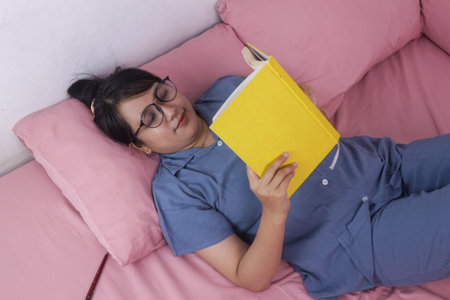 Young woman reading book while lying on the bed