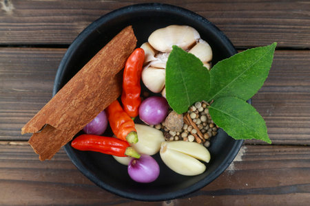 top view of various cooking spices such as chili, onion, garlic, cinnamon, pepper, lime leaves in a...
