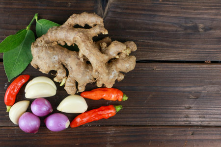 top view of various cooking spices such as chili, onion, garlic, pepper, ginger, lime leaves on wooden plank background, copy spaceの写真素材