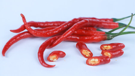 Fresh red chili peppers with green stems lying isolated on a white background