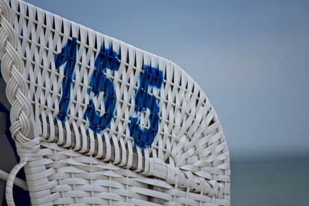 Number 155 stencilled in blue on a white painted wicker beach chair overlooking the ocean in close upの写真素材